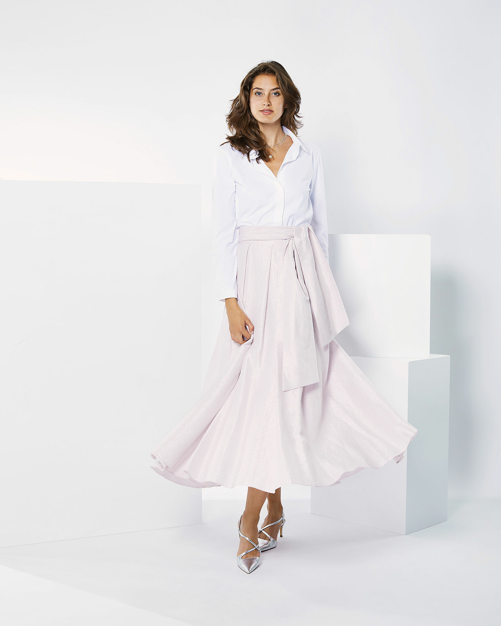 A brown hair model in rosy skirt and a white blouse is moving in a white setting