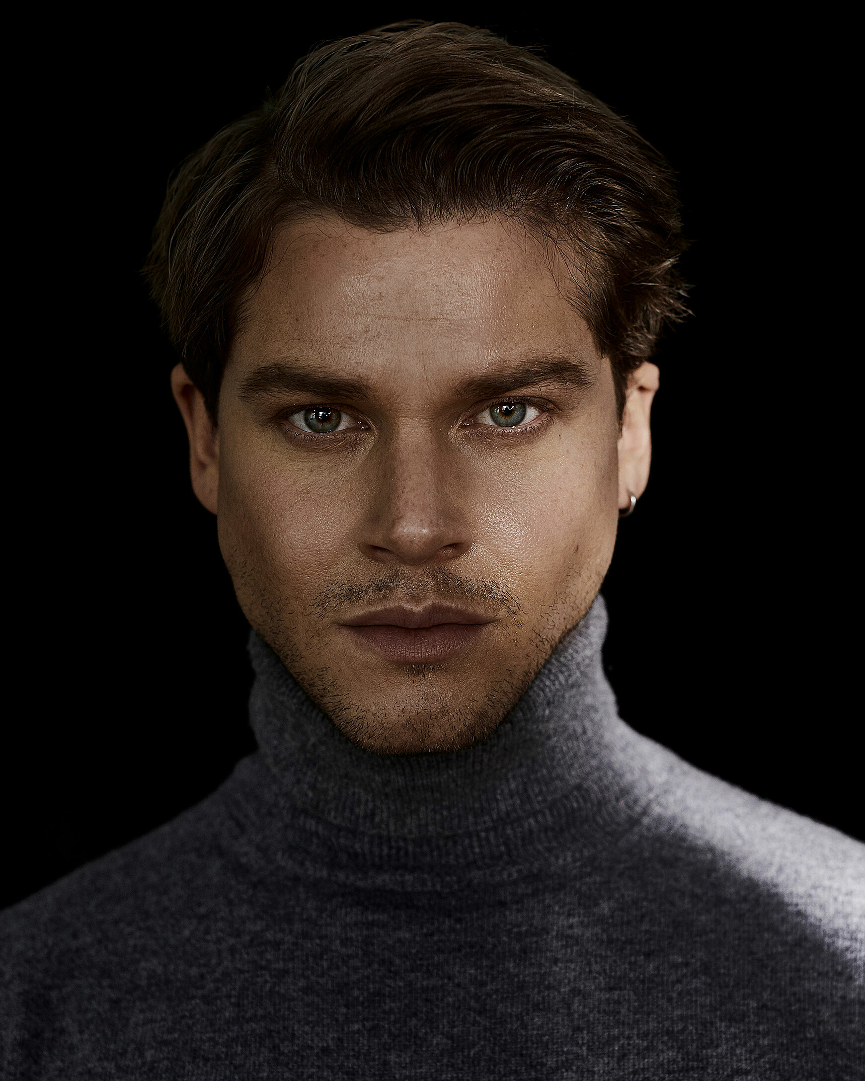 A portrait of a male model who wears a grey pullover with a turtle neck.