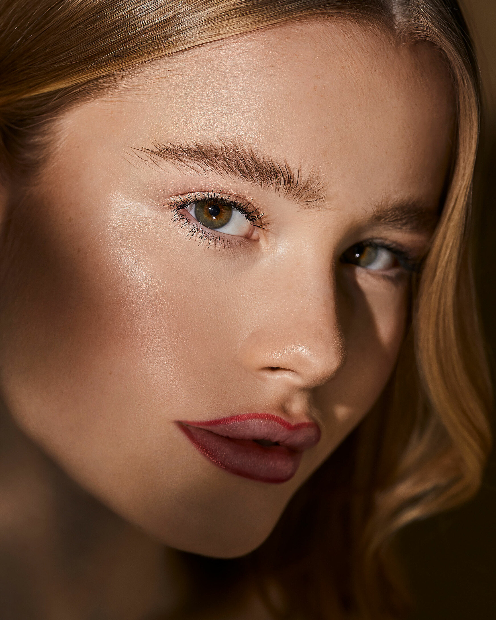 A close-up of a blonde female model. She wears red lipliner around her lips. 