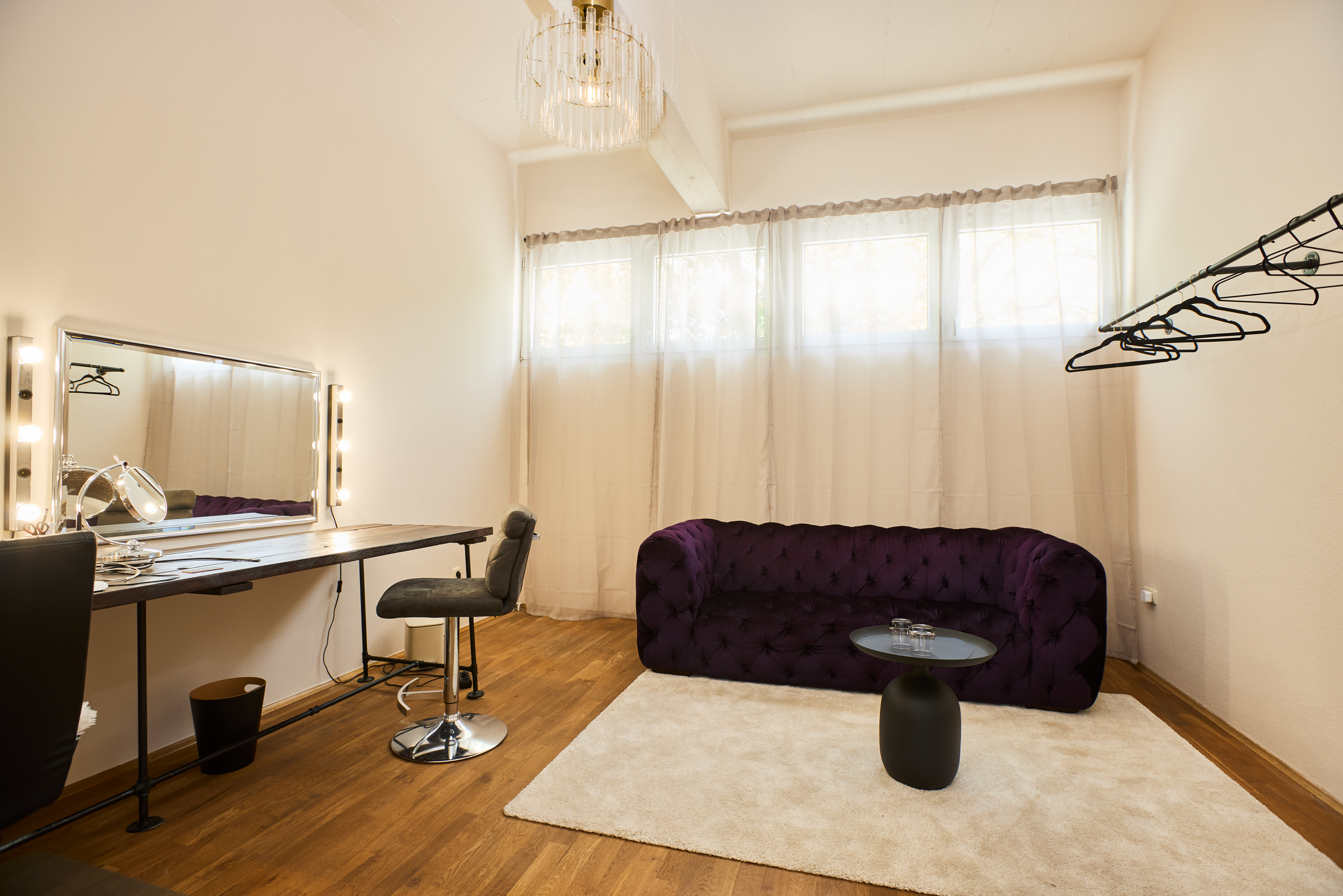 Makeup and dressing area with lighted vanity mirror and purple velvet sofa