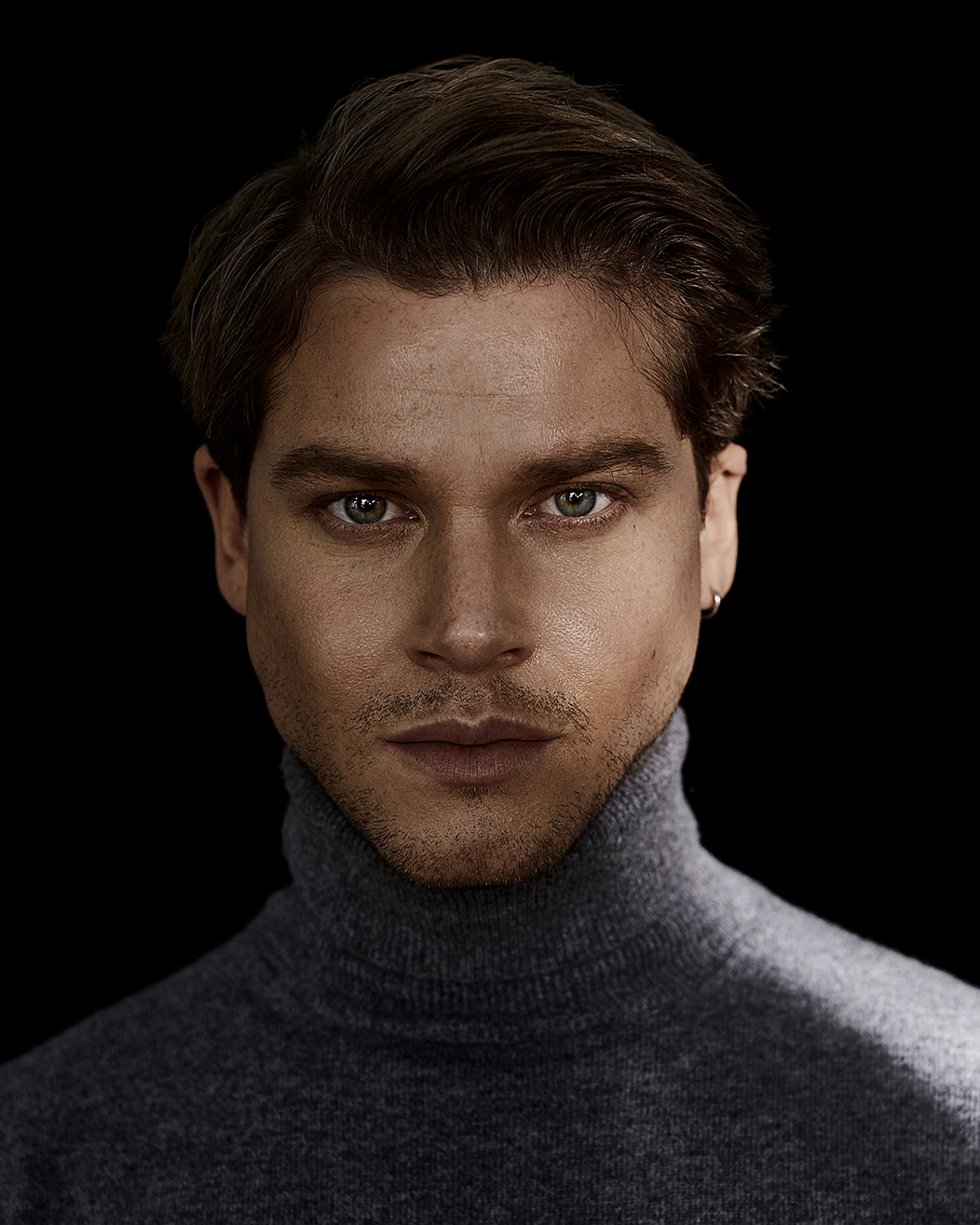 A portrait of a male model who wears a grey pullover with a turtle neck.