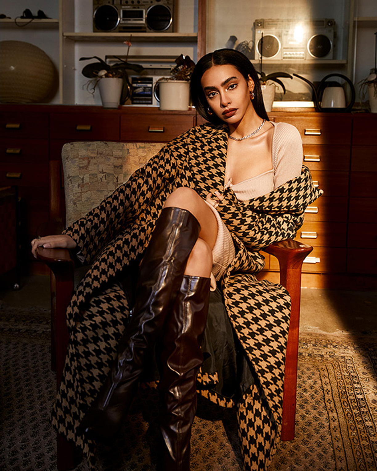 A model sit on the chair with a checkered coat and long brown boots