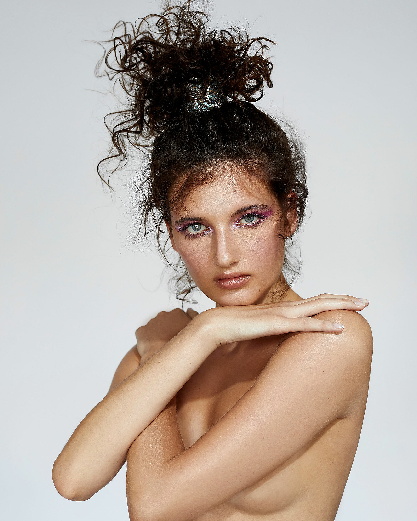 A beauty photography of a female model with dark curly hair in a bun. Her arms covering her skin.
