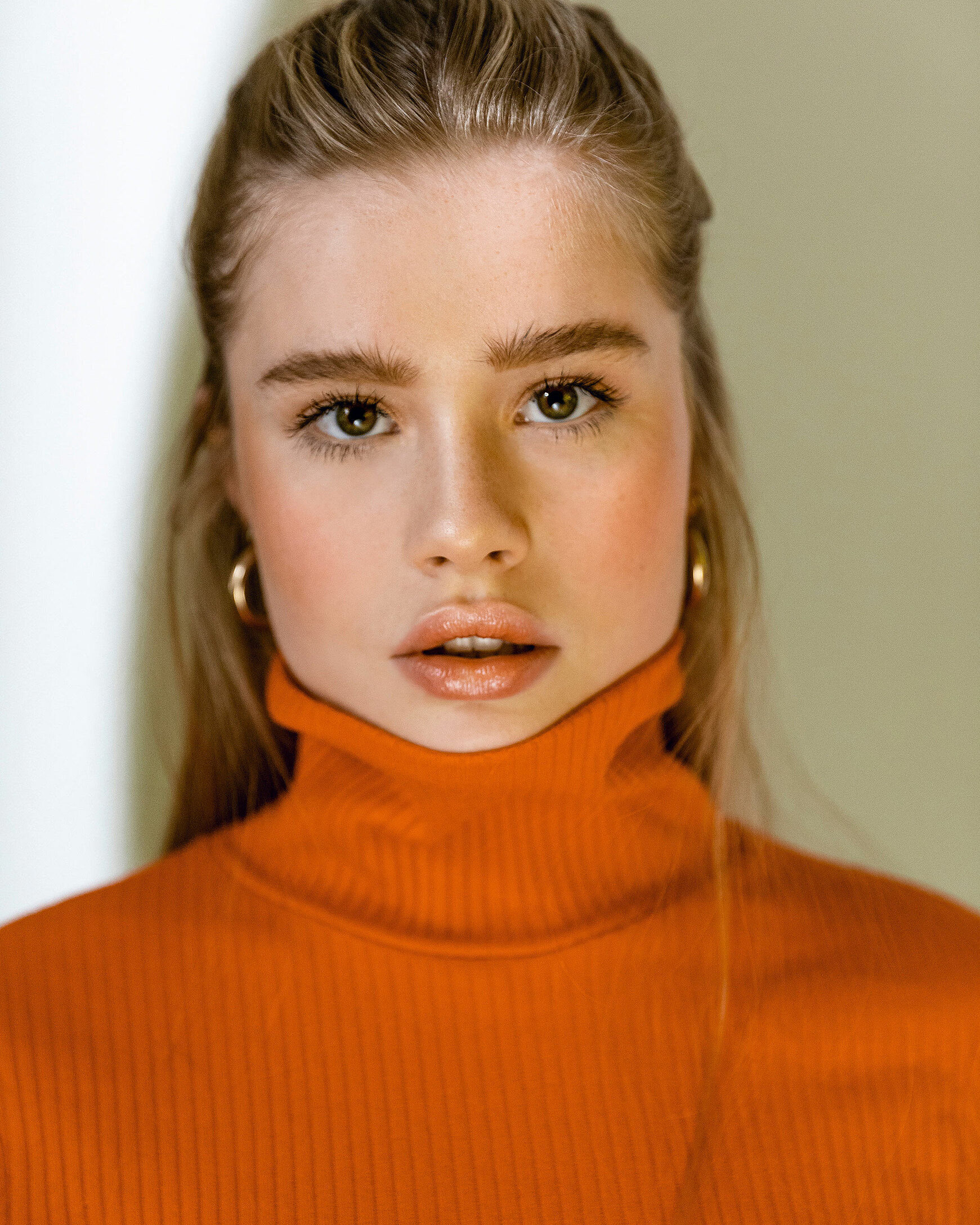 A portrait of a female blonde model with a orange turtleneck pullover with a gaze view in the camera