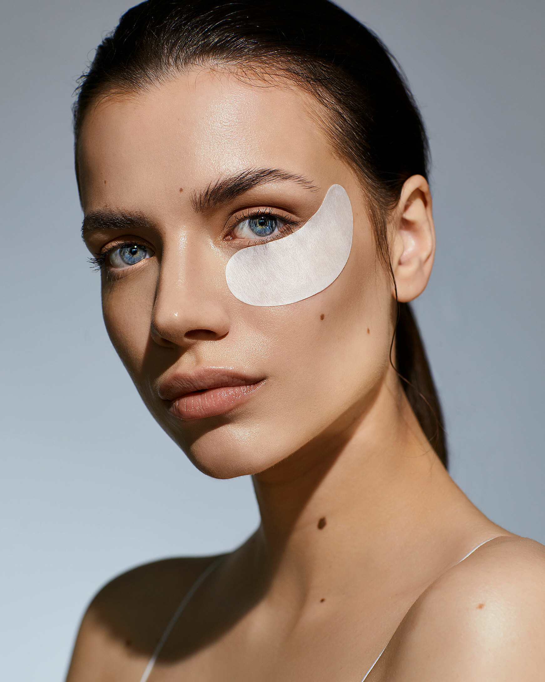 A beauty photography of a female model with dark hair. She wears a white eyepad