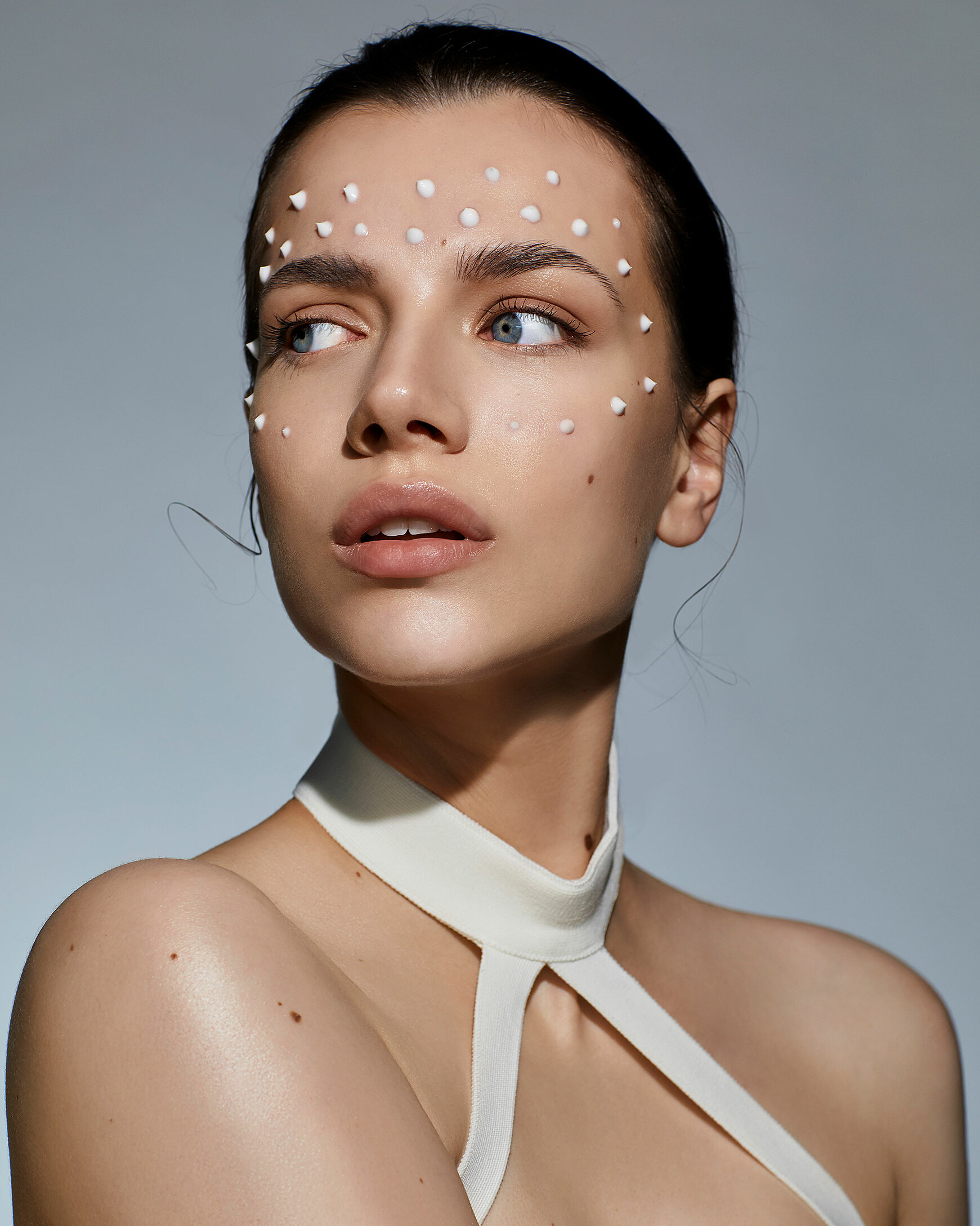 A beauty photography of a female model with dark hair. She has cream dots around her eyes