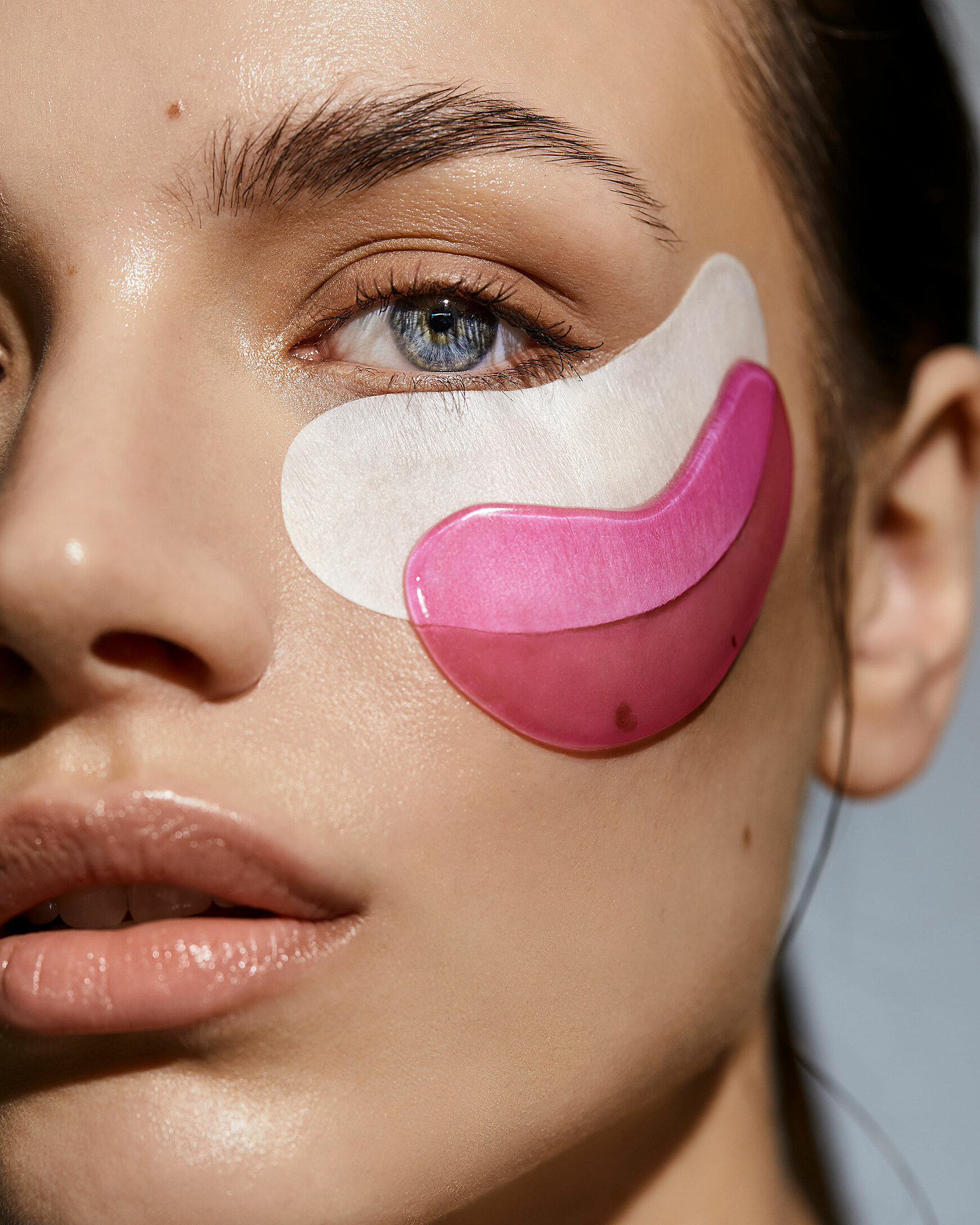 A beauty photography of a female model with dark hair. She wears two eye pads one upon the other 