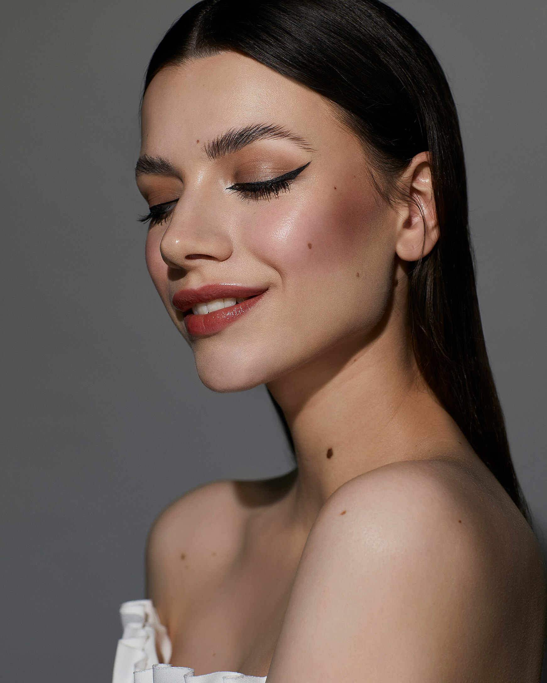 A beauty photography of a female model with dark hair. She wears a red lips and a white top. The eyeliner is in the focus.