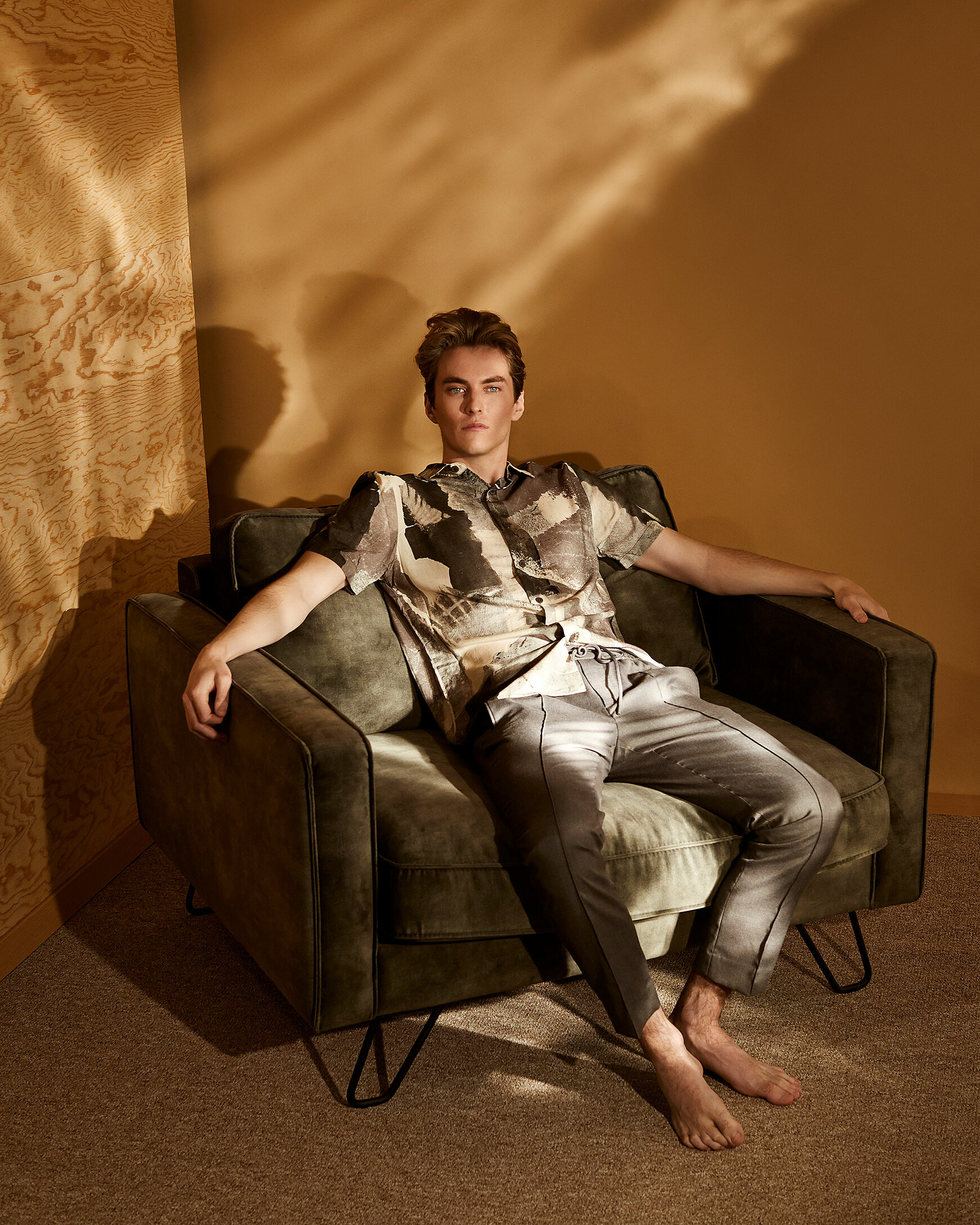 A male model sits on a chair with military green clothes.