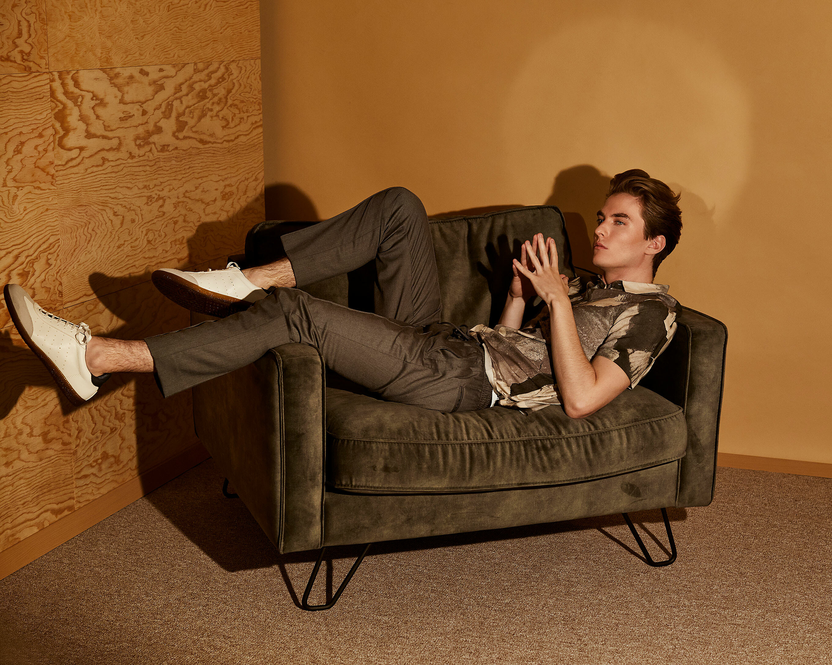 A male model sits on a chair with military green clothes.