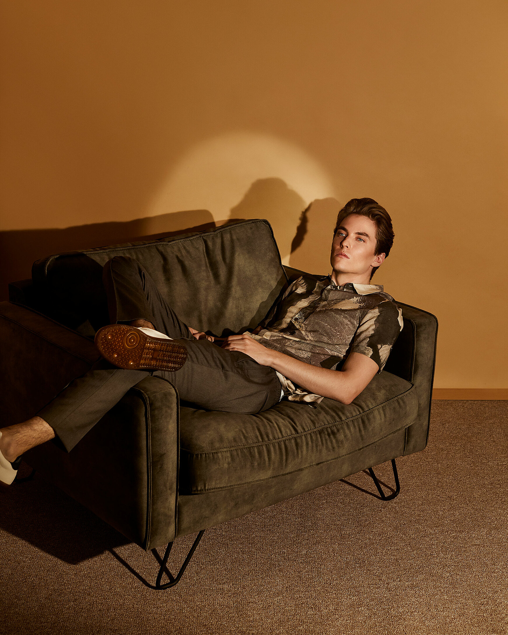 A male model sits on a chair with military green clothes.