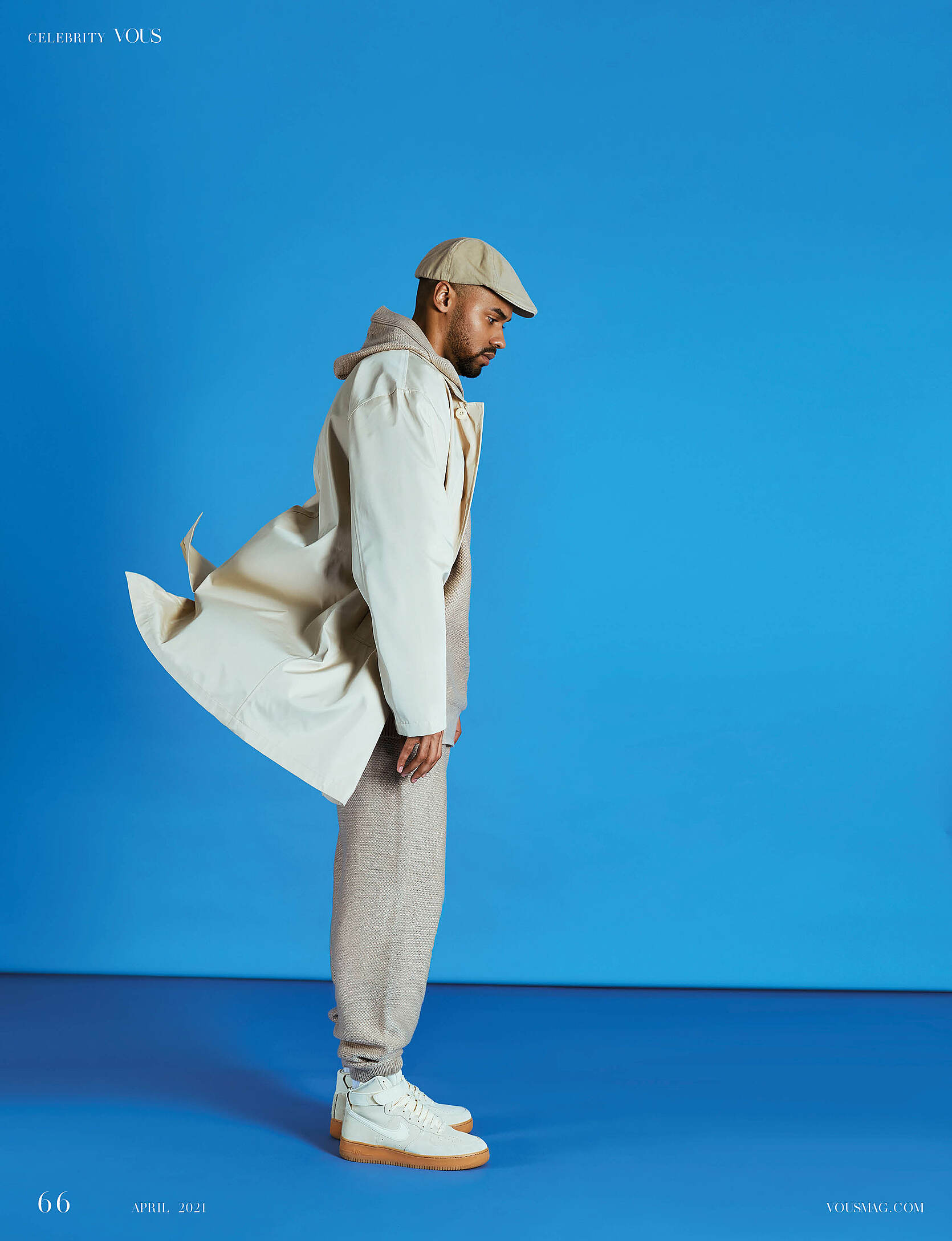 A male model in front of a blue background with a beige coat and a beige hat