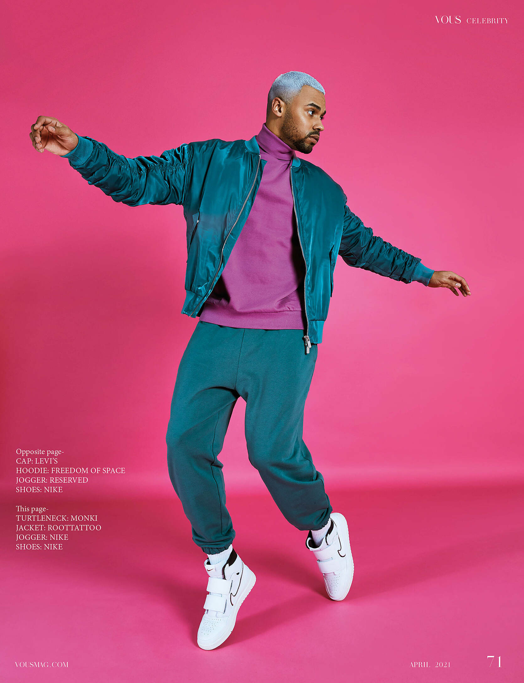 A male model with white hair in green trousers and green jacket. He wears a purple pullover with a turtleneck and white sneakers