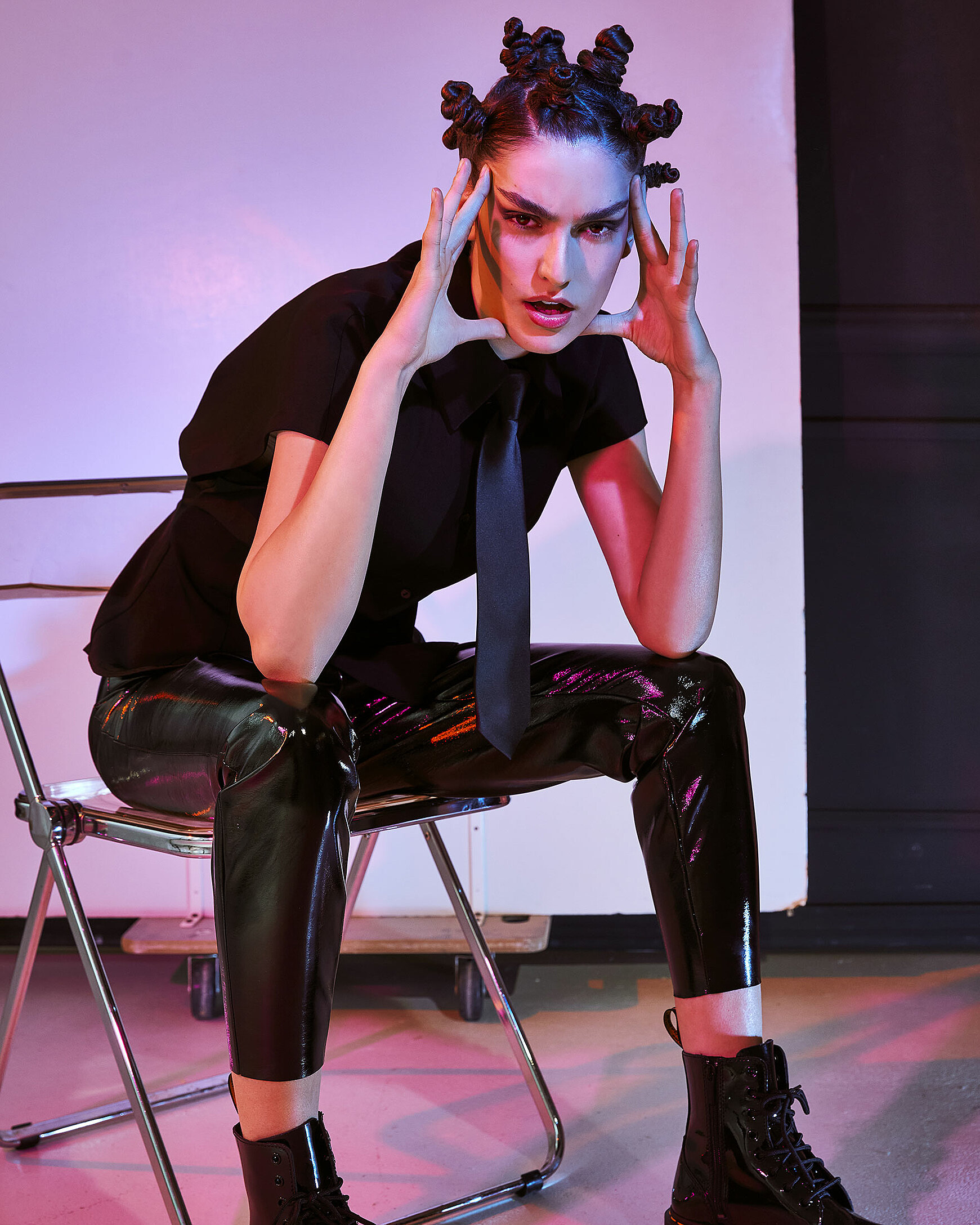 A female model sits on a transparent chair illuminated with red/ pink light in black clothes