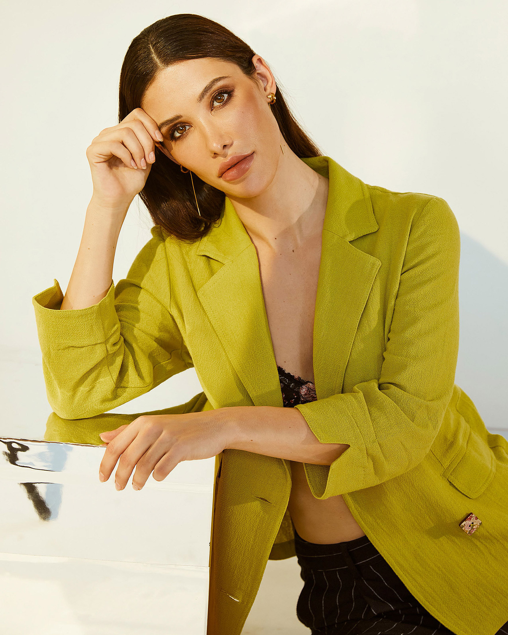 A female model sits on the ground and lean against a mirror cube in a light kiwi green jacket