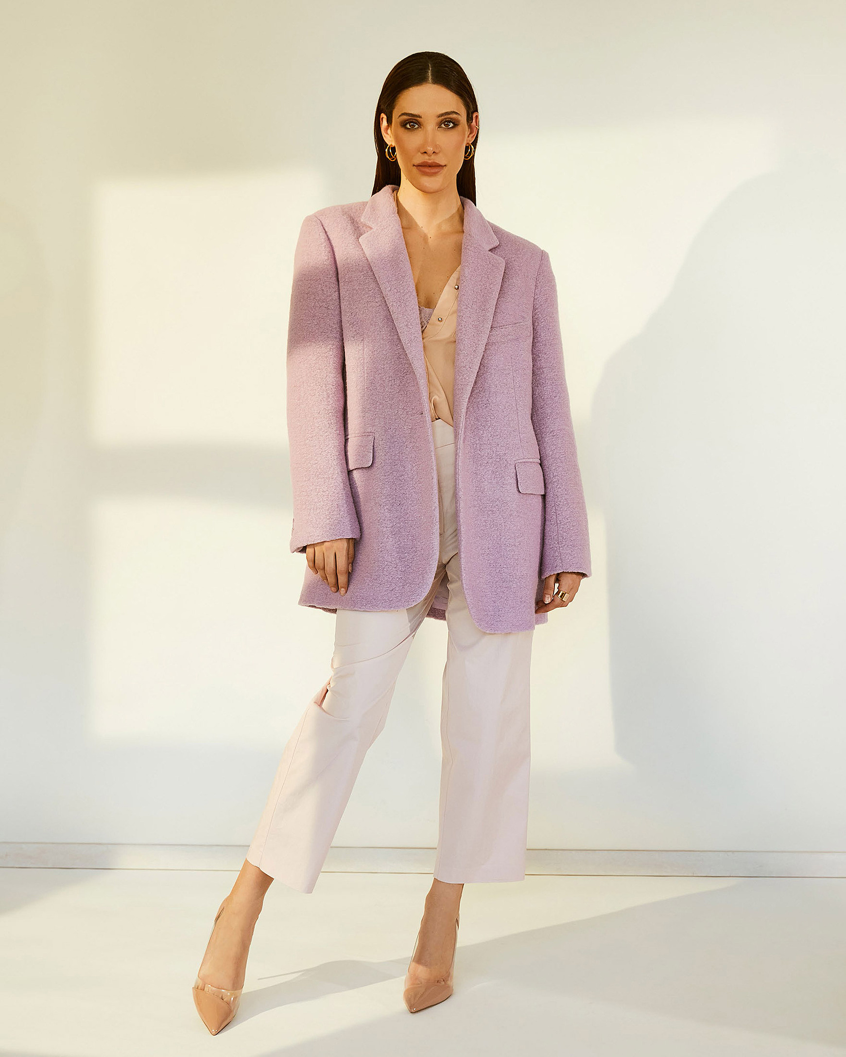 A female model stands in the light of the windows in the lilac coat