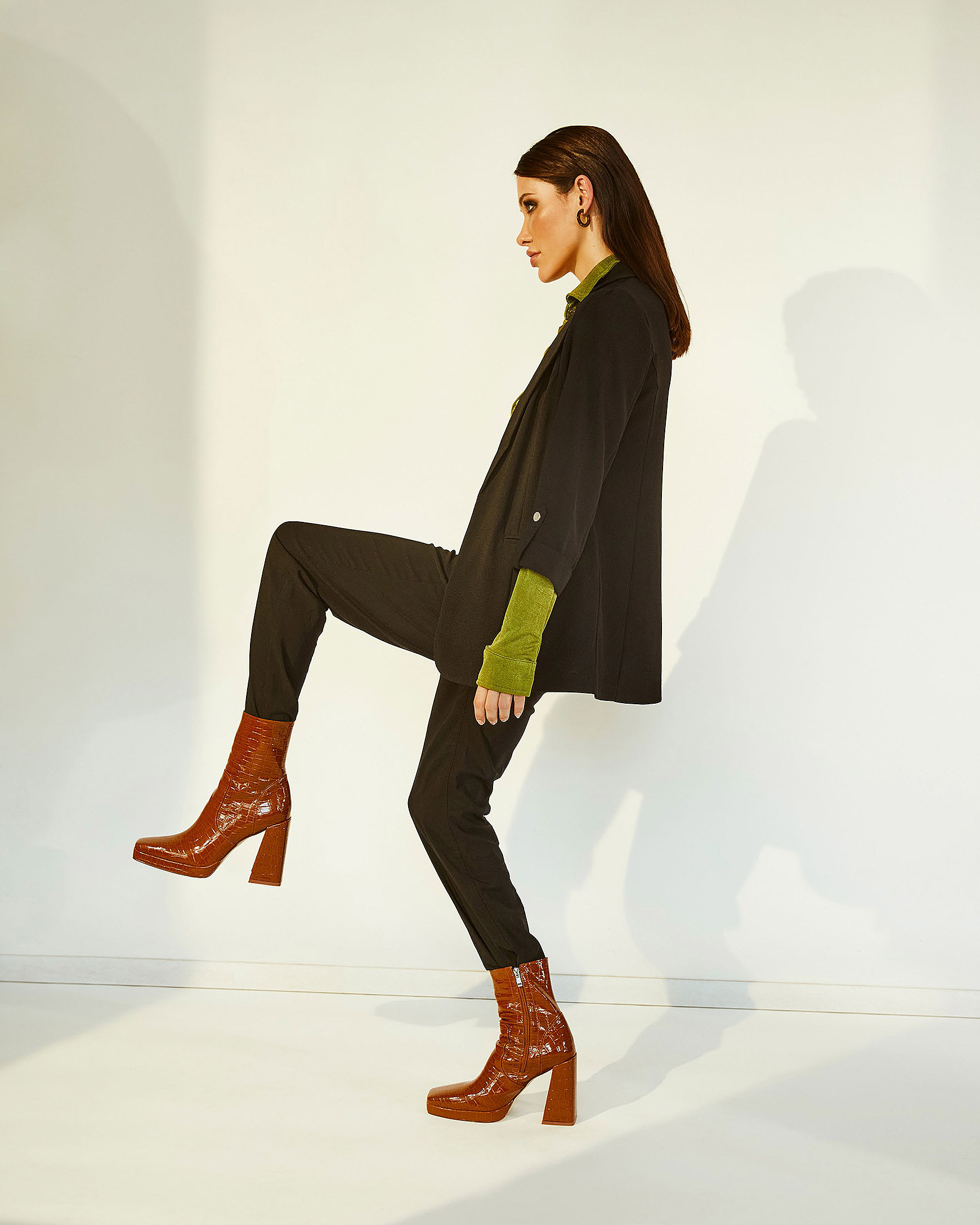 A female model in a green blouse, black jacket and trousers with brown boots