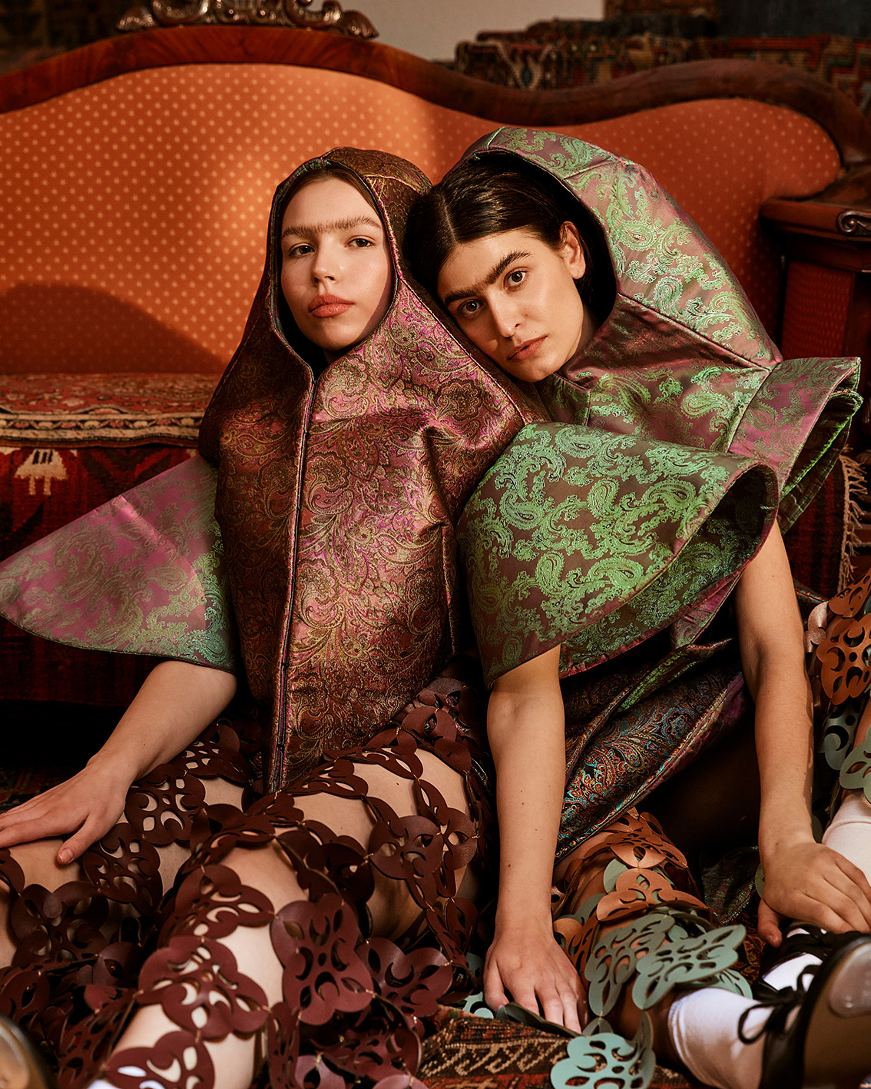 two models sit on the floor in front of a sofa