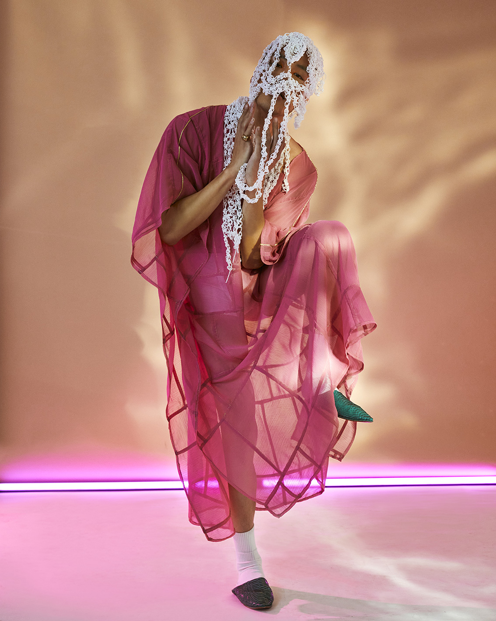 a model in a colorful set with pink light pose in a pink dress with a white headpiece