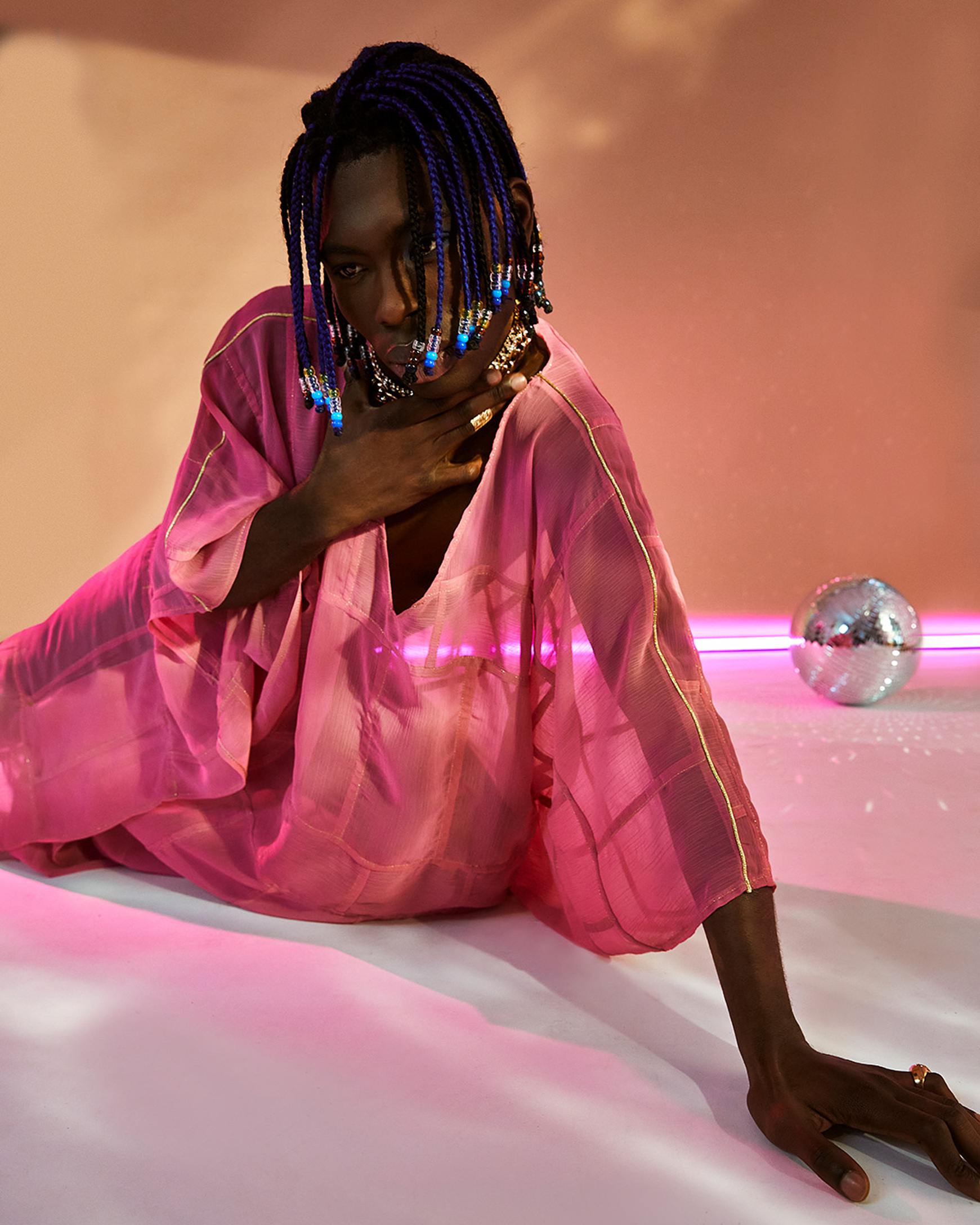 a model in a colorful set with pink light pose on the floor in a pink dress