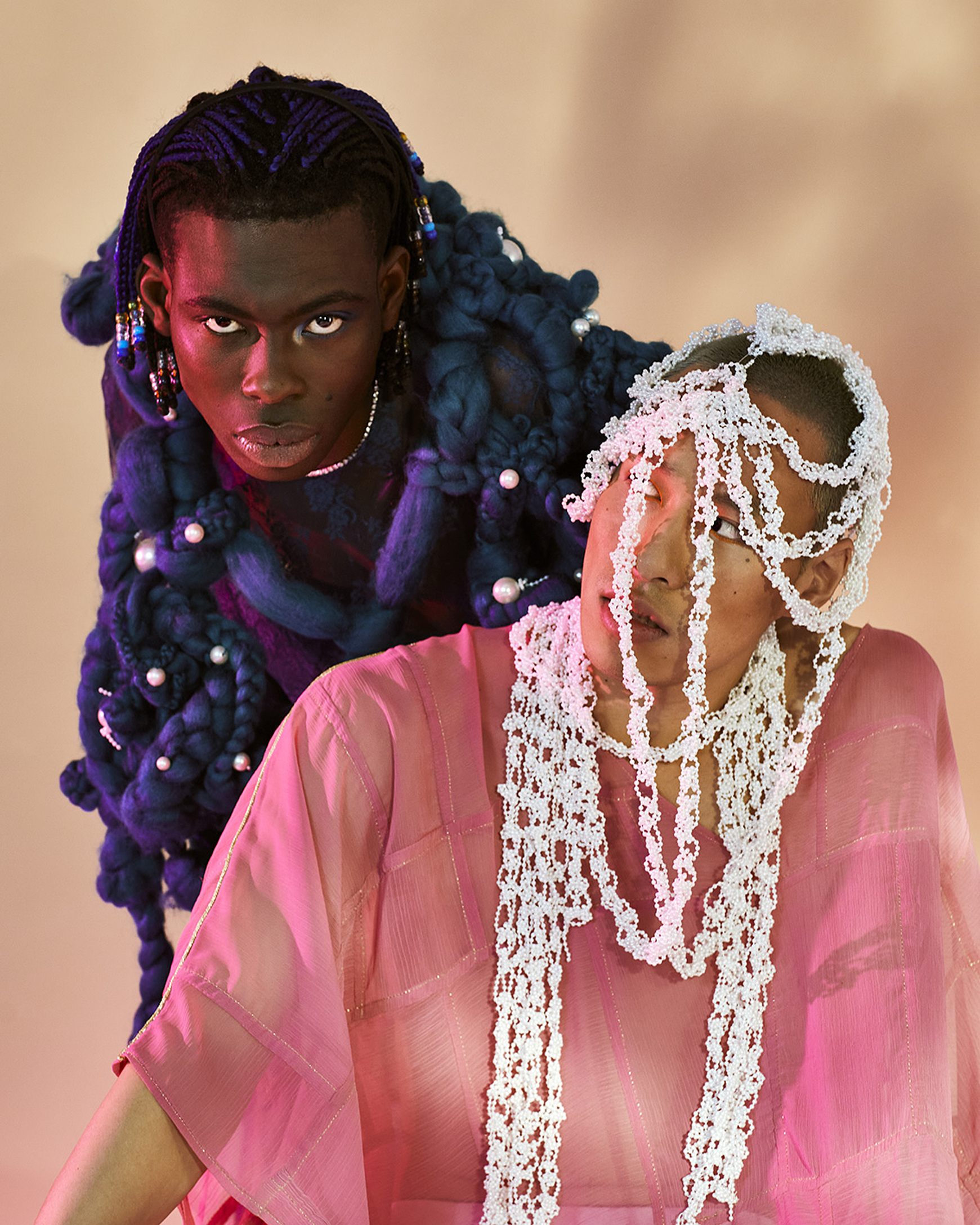 a portrait of two models in blue and pink fashion. One of them wears a white headpiece