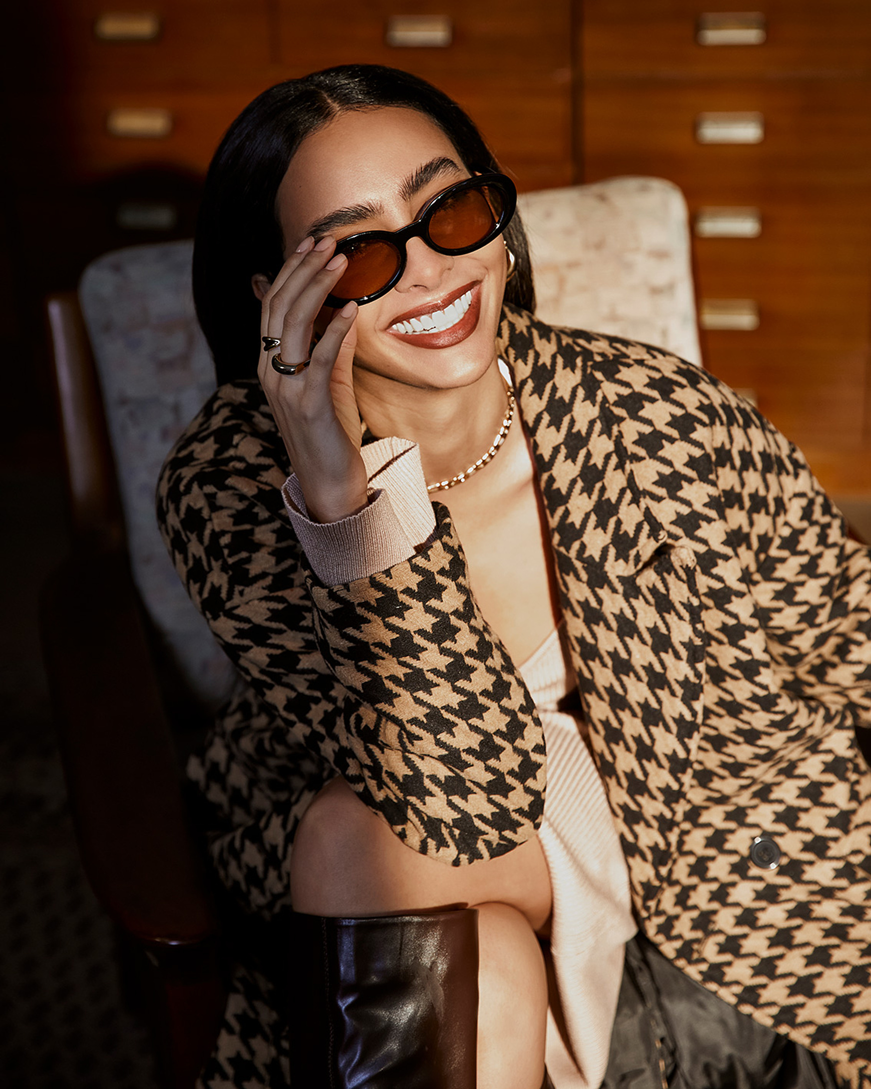 a model smile in the camera with dark sunglasses and a checkered coat