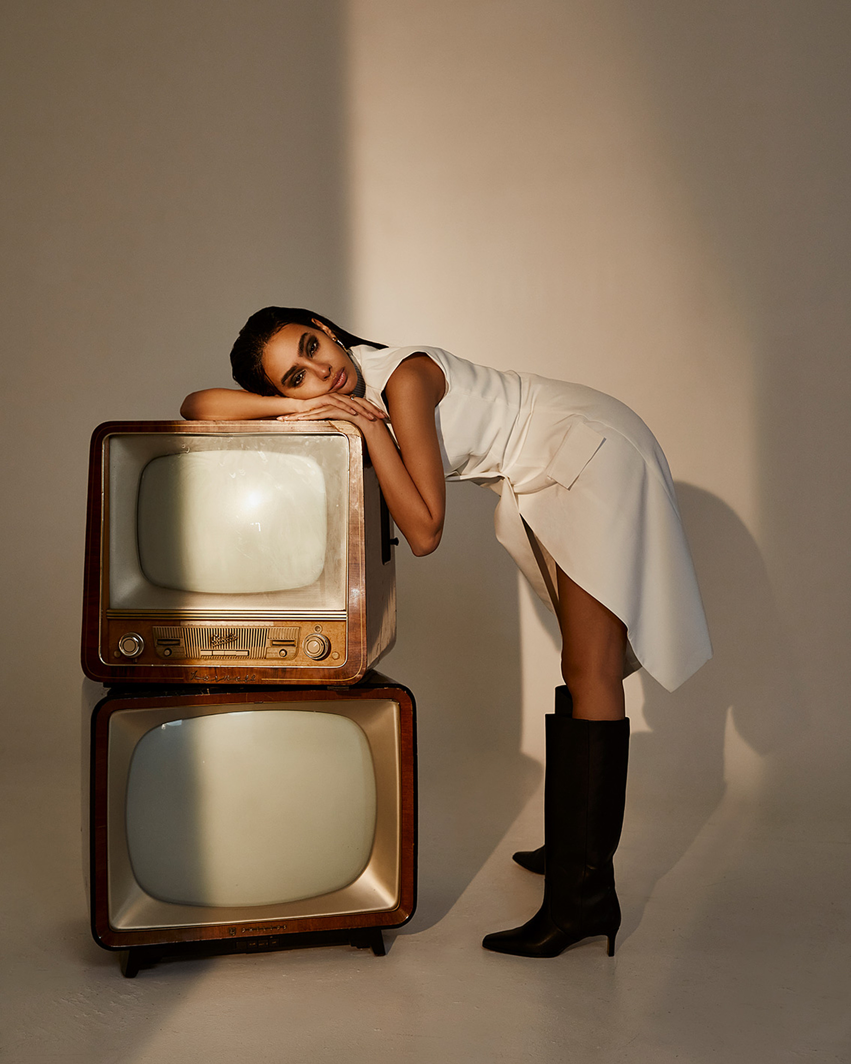 A model lean on stacked televisions in a white dress