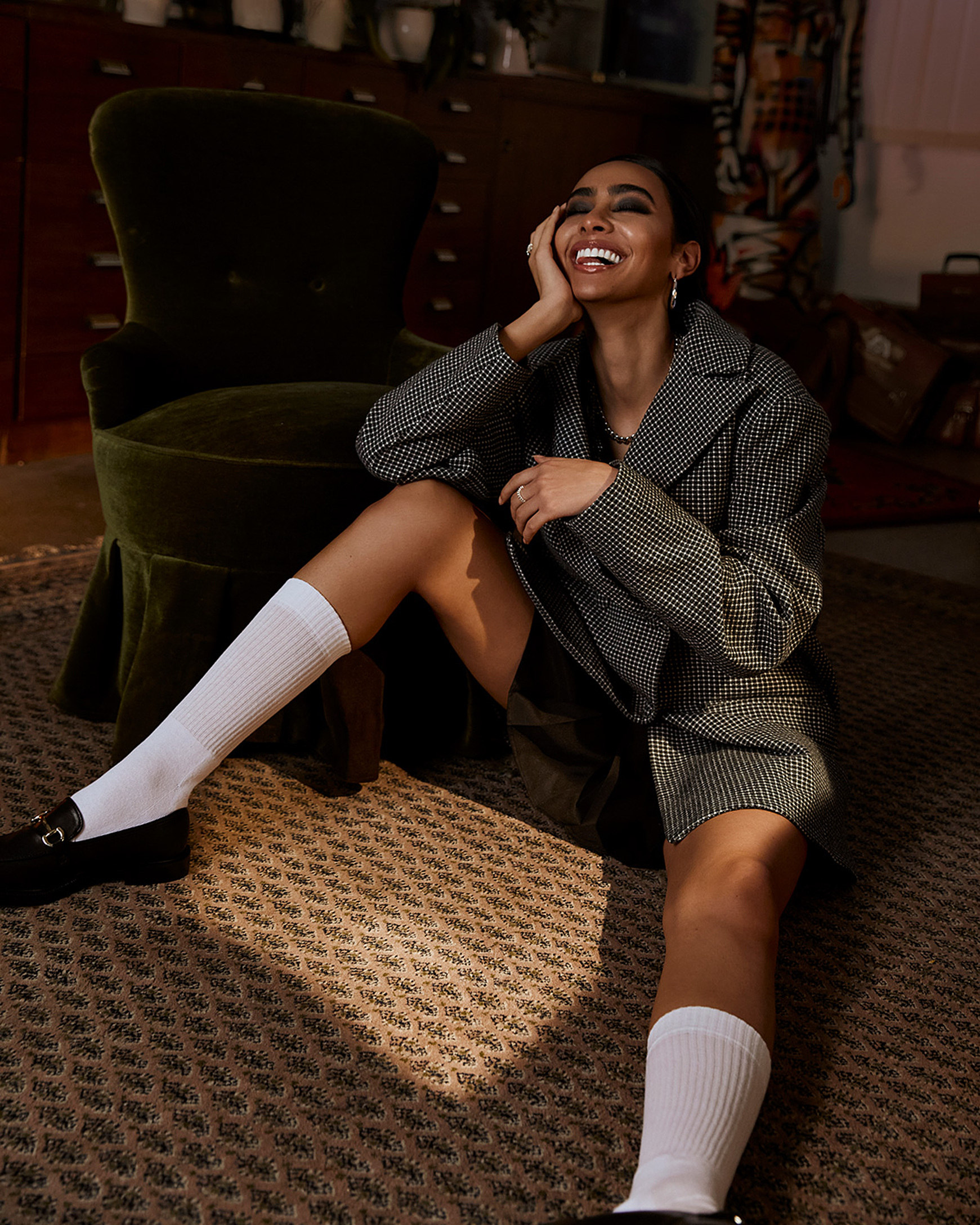 a model sits on the floor with a big smile in a blazer and white long socks