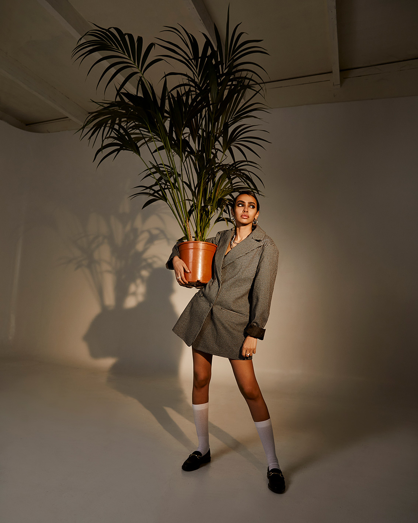 A model caring a big green plant in a blazer and white long socks