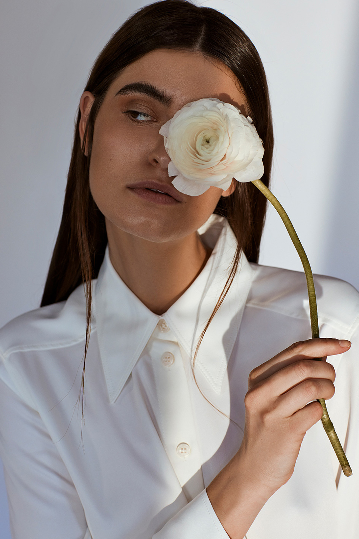 A female model in a white blouse holding a white flower