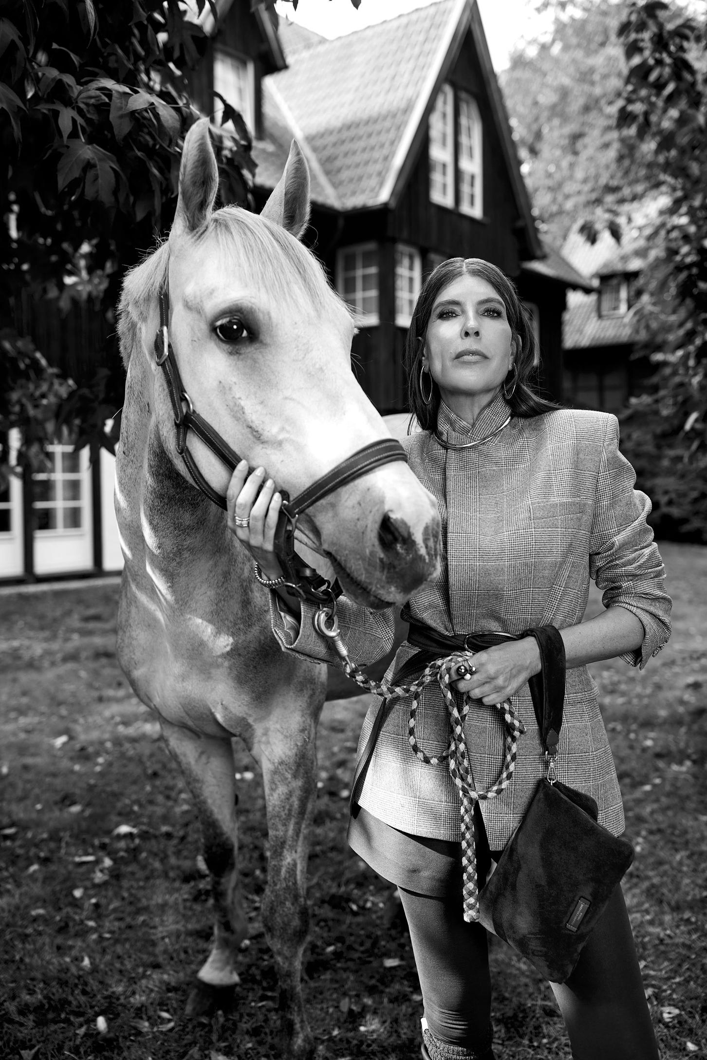 Ein schwarz weiss Bild einer Frau mit einem weissen Pferd. Darauf trägt sie einen Blazer