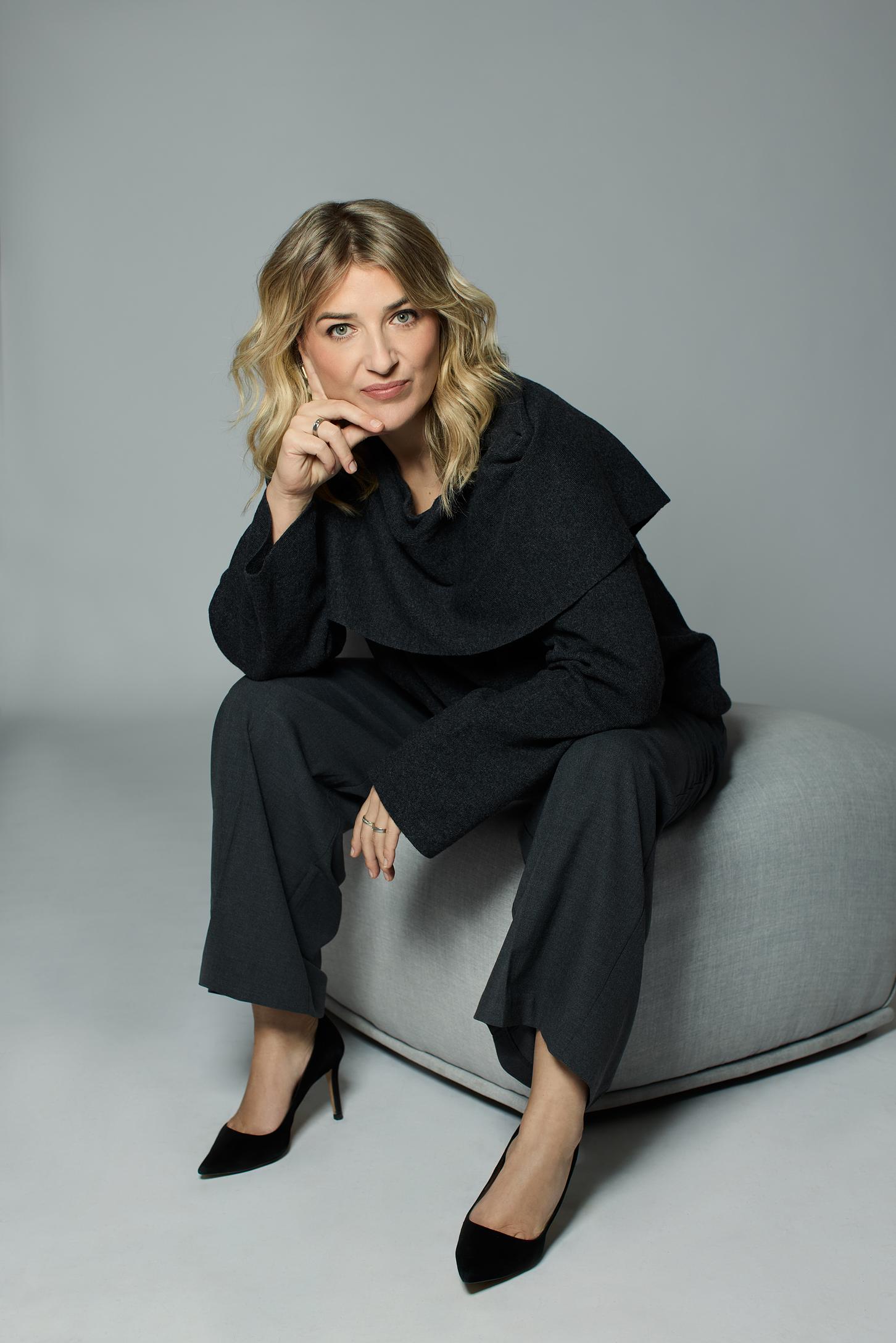 Unternehmerin in einem grauen Outfit sitzt auf einem hellgrauen Sessel