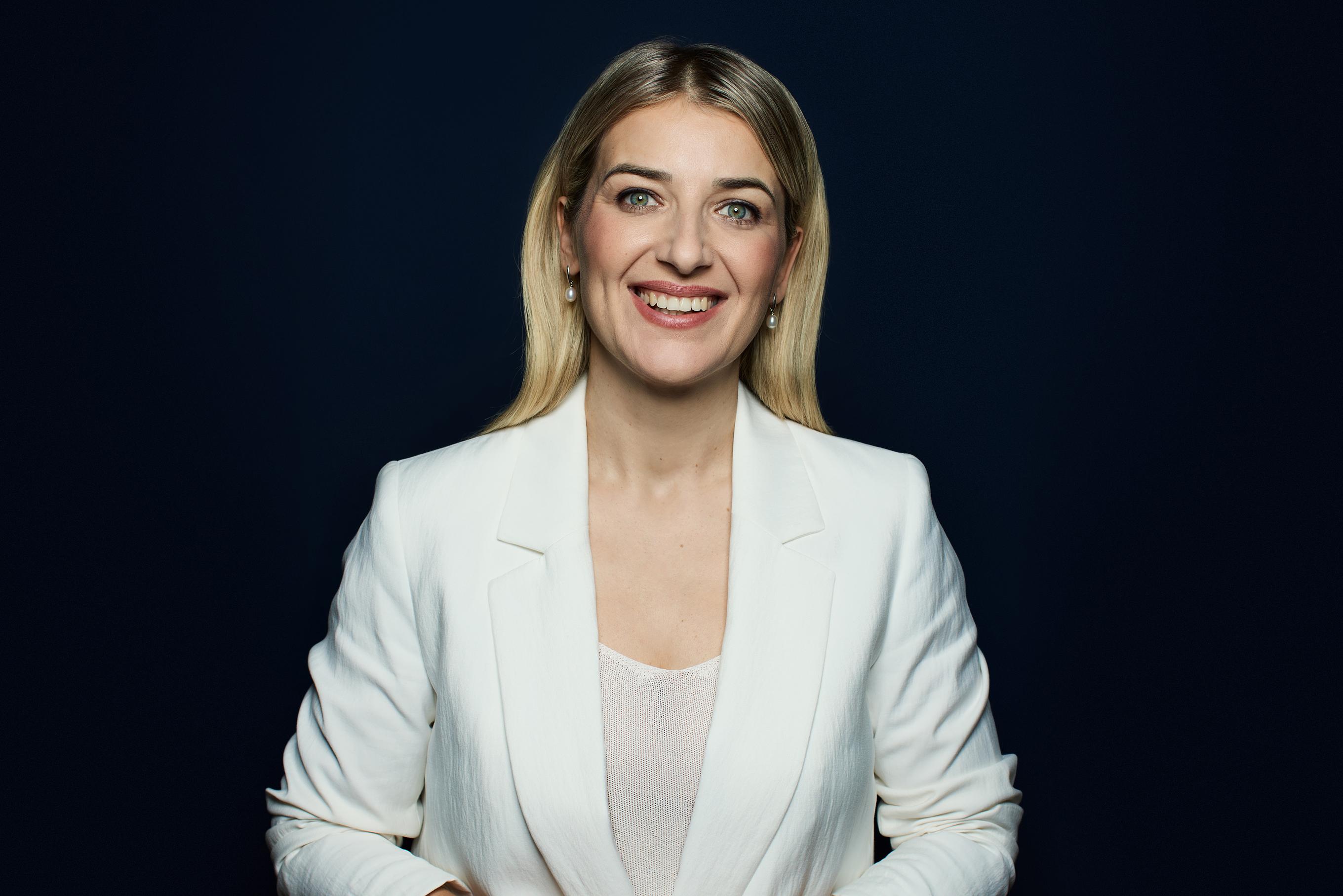 Unternehmerin in weisser Kleidung vor einem dunkel blauen Hintergrund