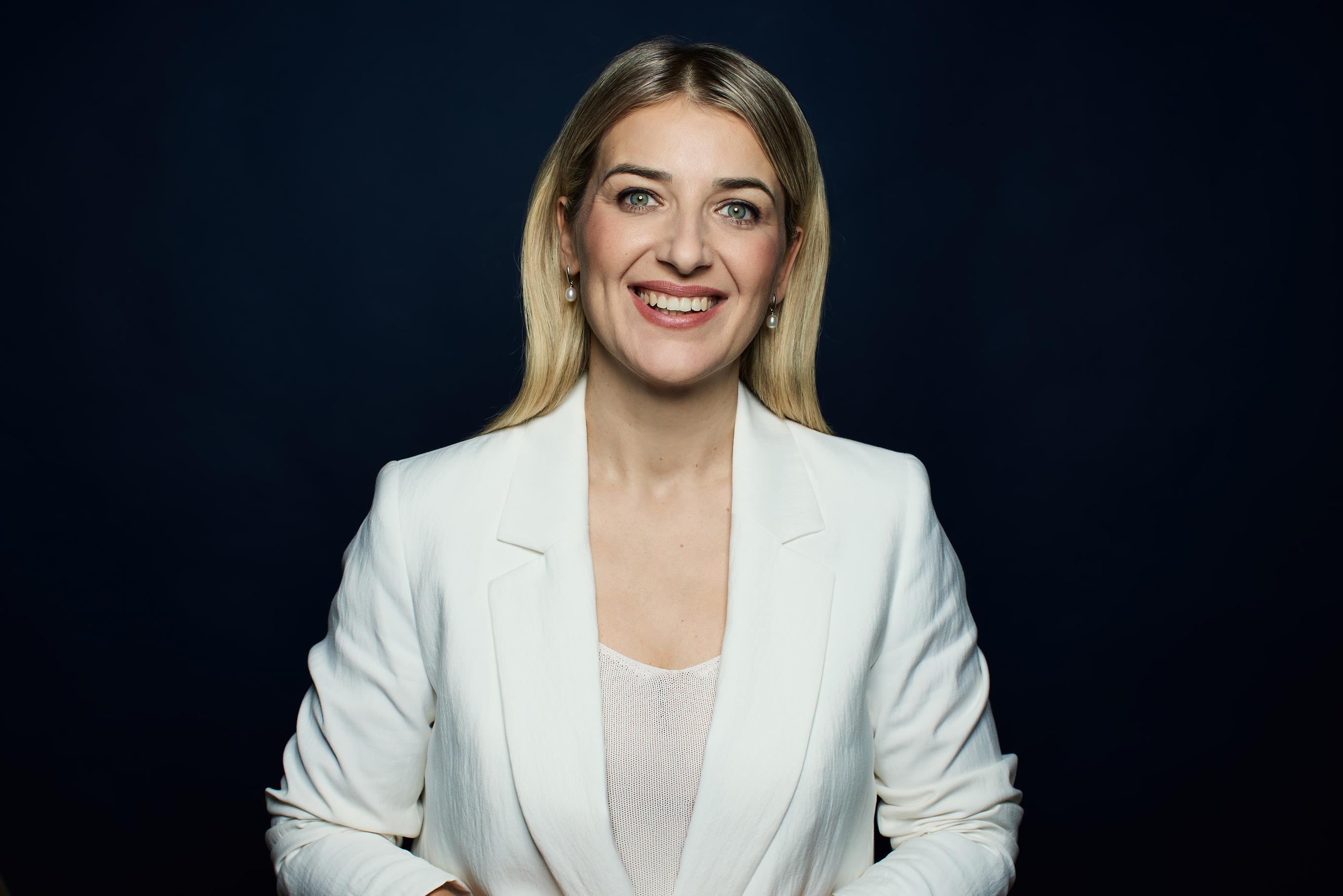 Unternehmerin in weisser Kleidung vor einem dunkel blauen Hintergrund