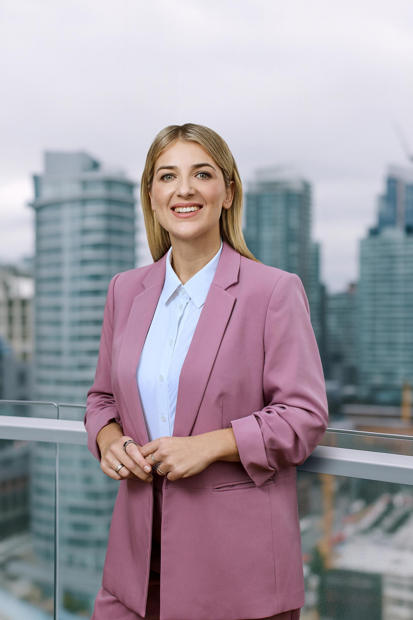 Frau im rosé farbigen Blazer steht draußen vor einer Skyline