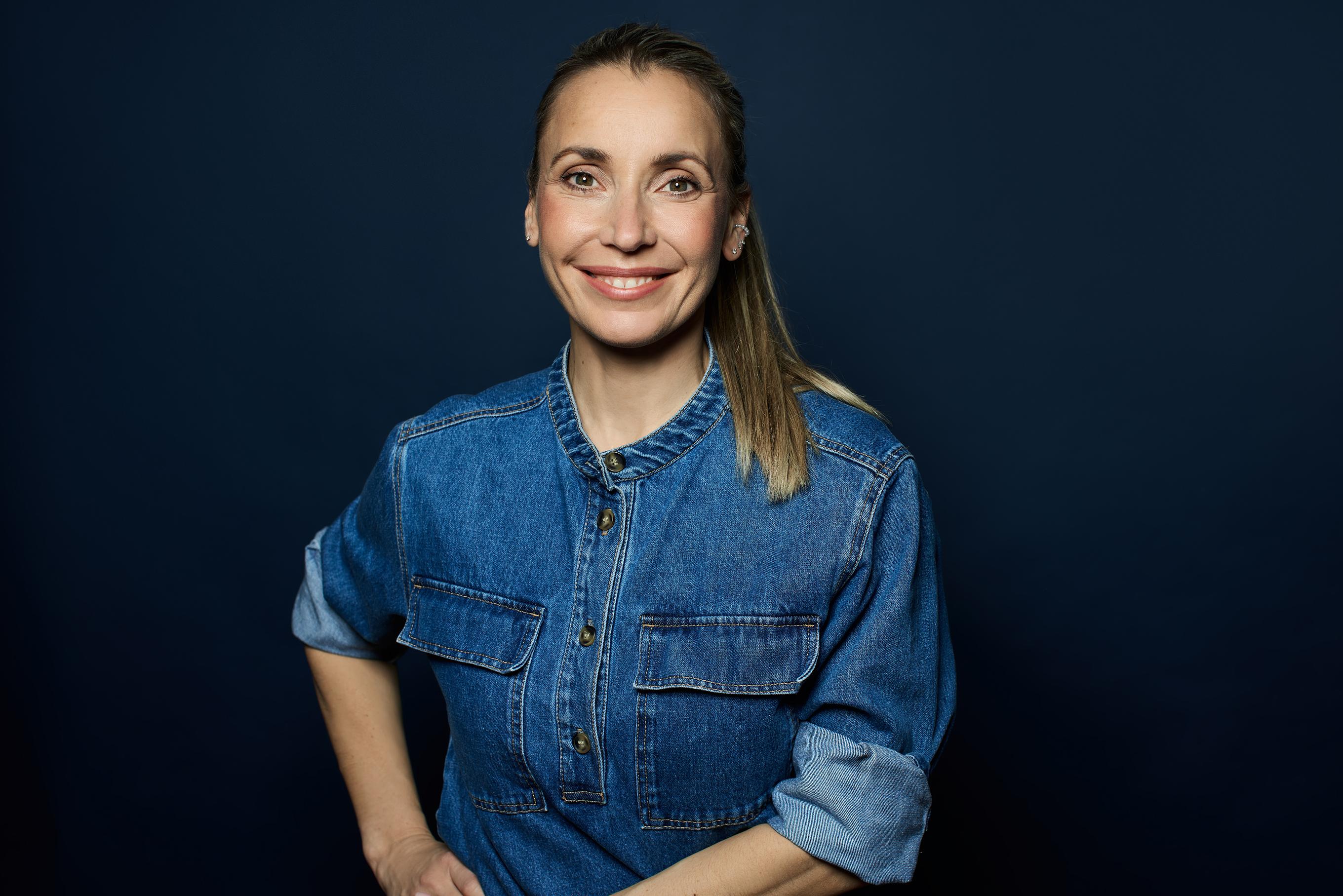 Unternehmerin steht vor einem dunkel blauen Hintergrund im Jeanshemd