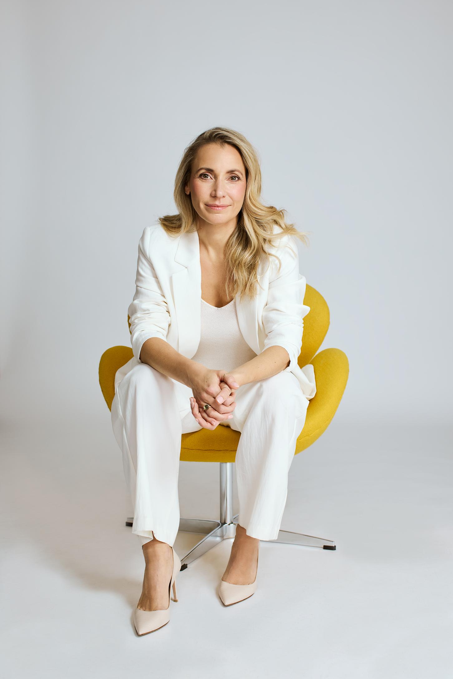 Unternehmerin sitzt im weißen Anzug auf einem gelben Stuhl