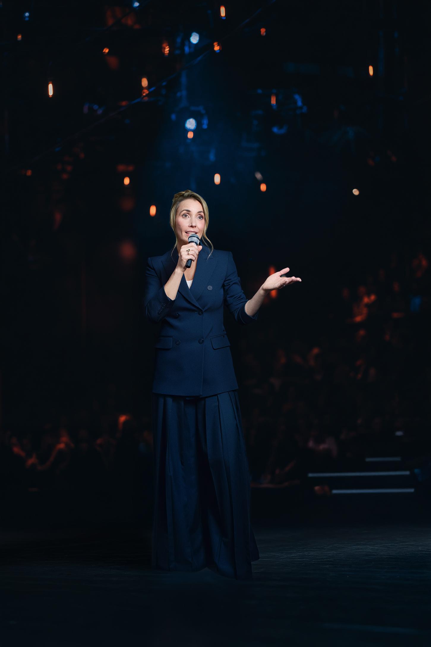 Unternehmerin steht auf der Bühne und hält einen Vortrag in einem dunklen Anzug